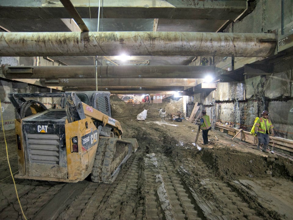 Workers use a bobcat to help grade the bottom of the station box, where waterproofing and an invert (floor) slab will be installed.