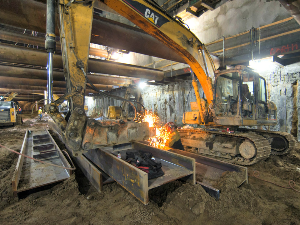 A project mechanic works on a jackhammer fitted to a large excavator inside the station box.